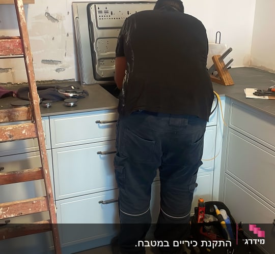 אדם עובד על התקנת תנור במטבח עם כלי עבודה